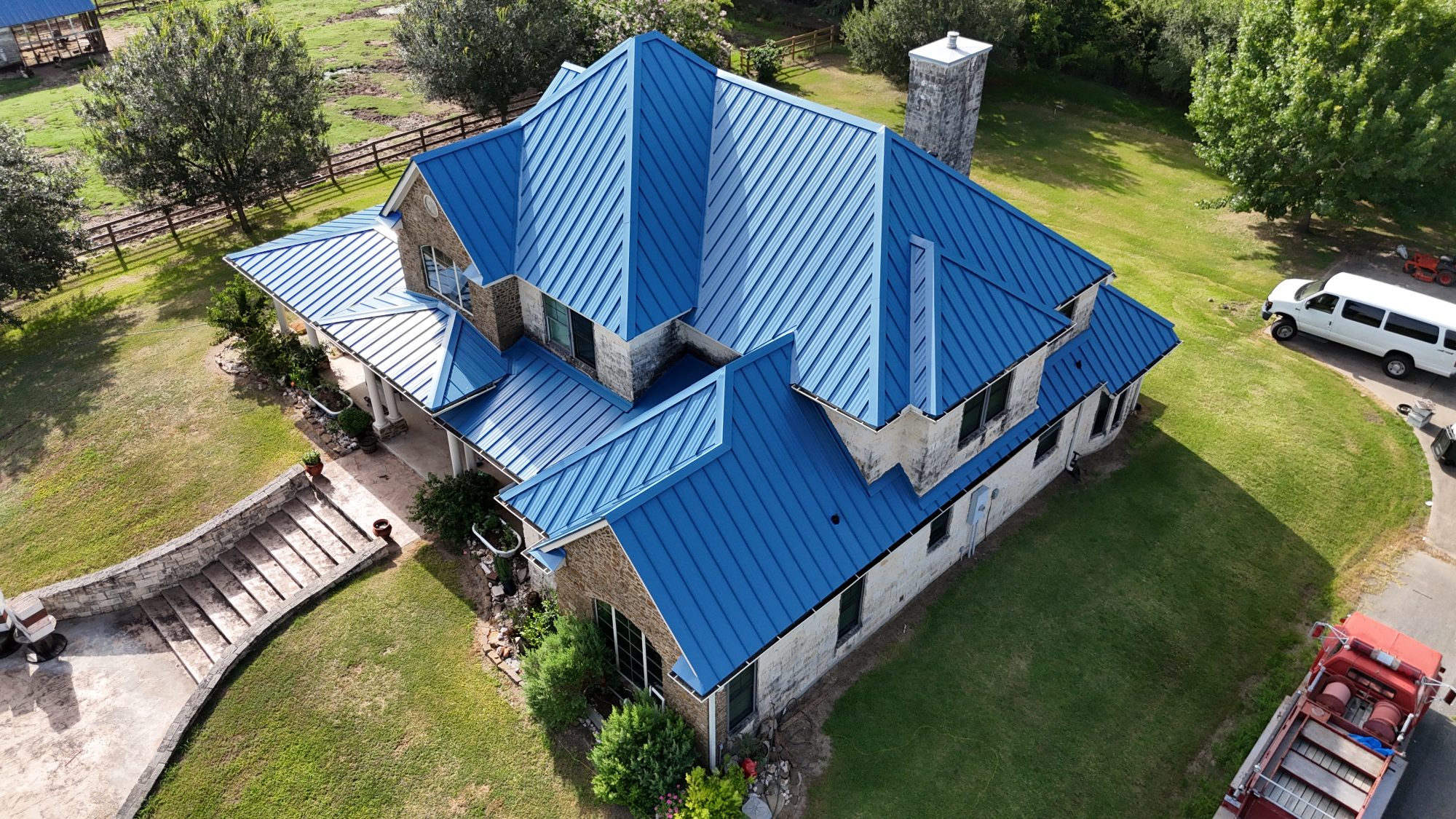 Blue standing seam metal roof with crew van in the drive, aerial