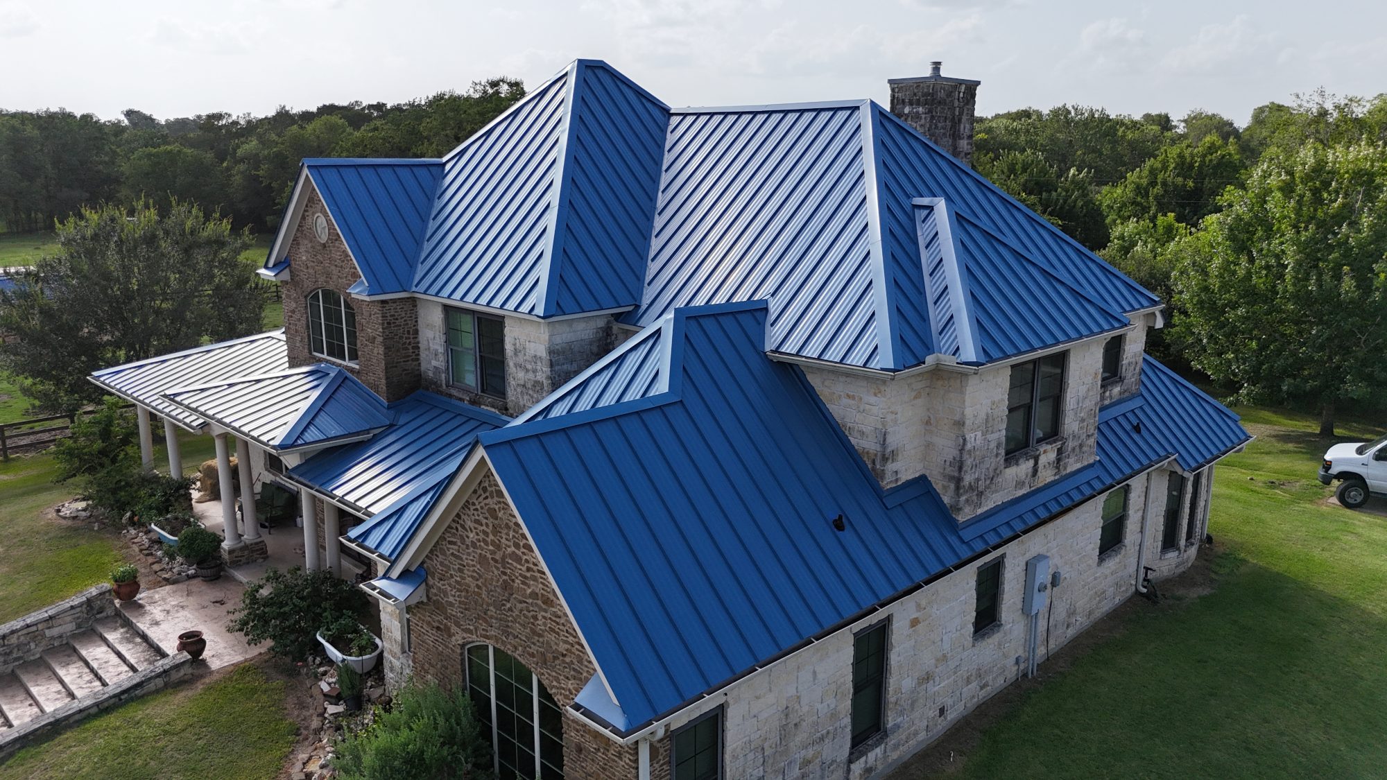 Blue standing seam metal roof on a stone home, aerial front