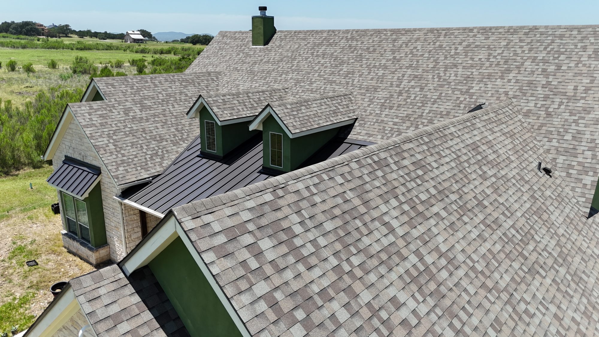 Grey architectural shingle roof with dormers on a green-trim home, aerial
