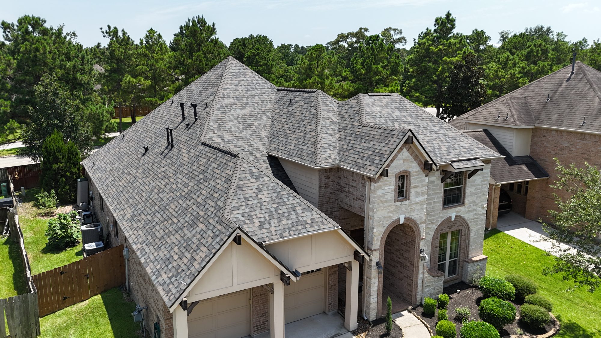Grey architectural shingle roof on a stone two-story home, aerial