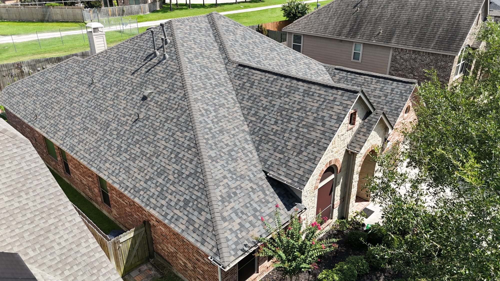 Grey shingle roof on a brick home with an arched entry, aerial