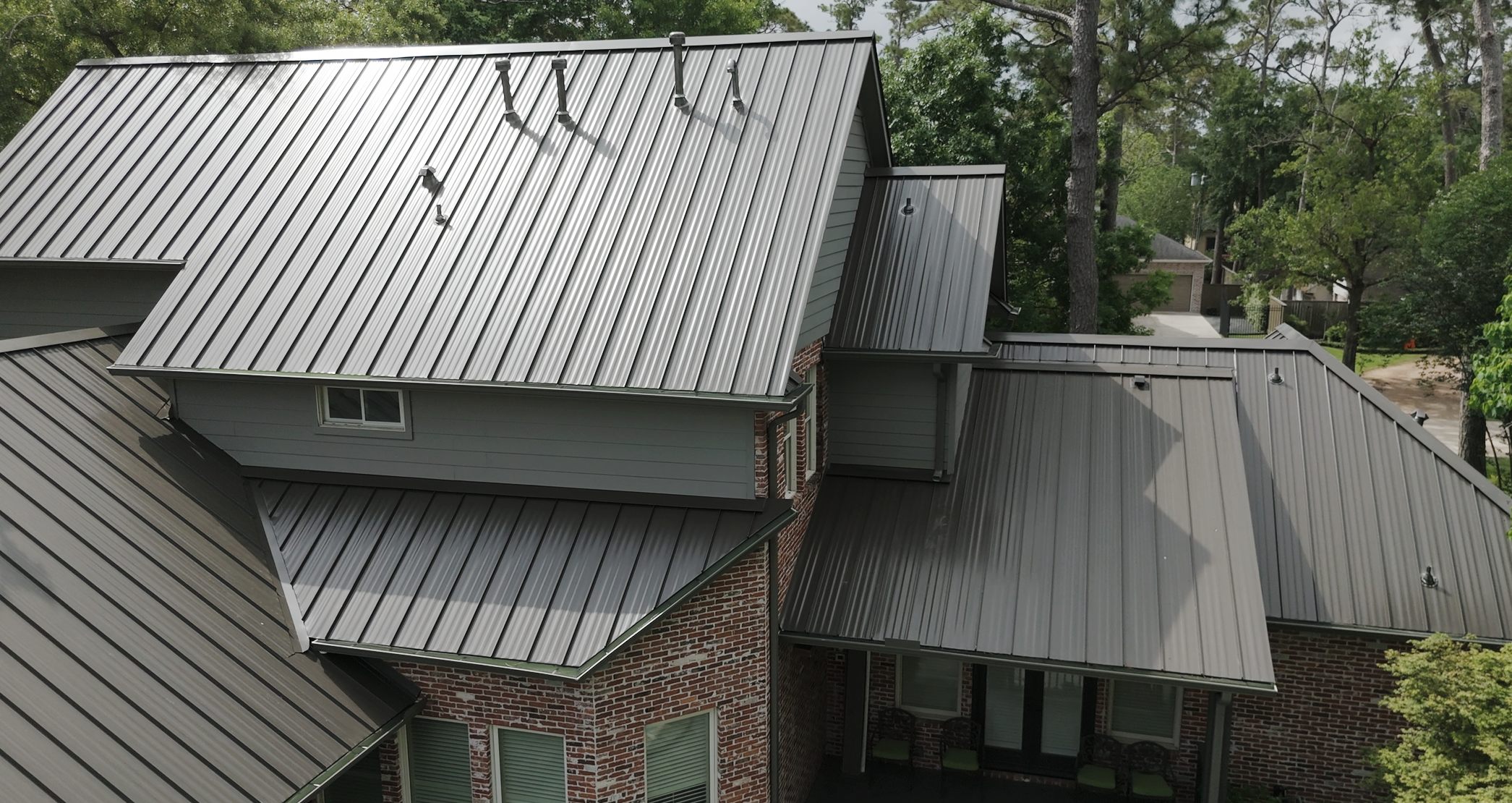 Grey standing seam metal roof on a brick home, aerial